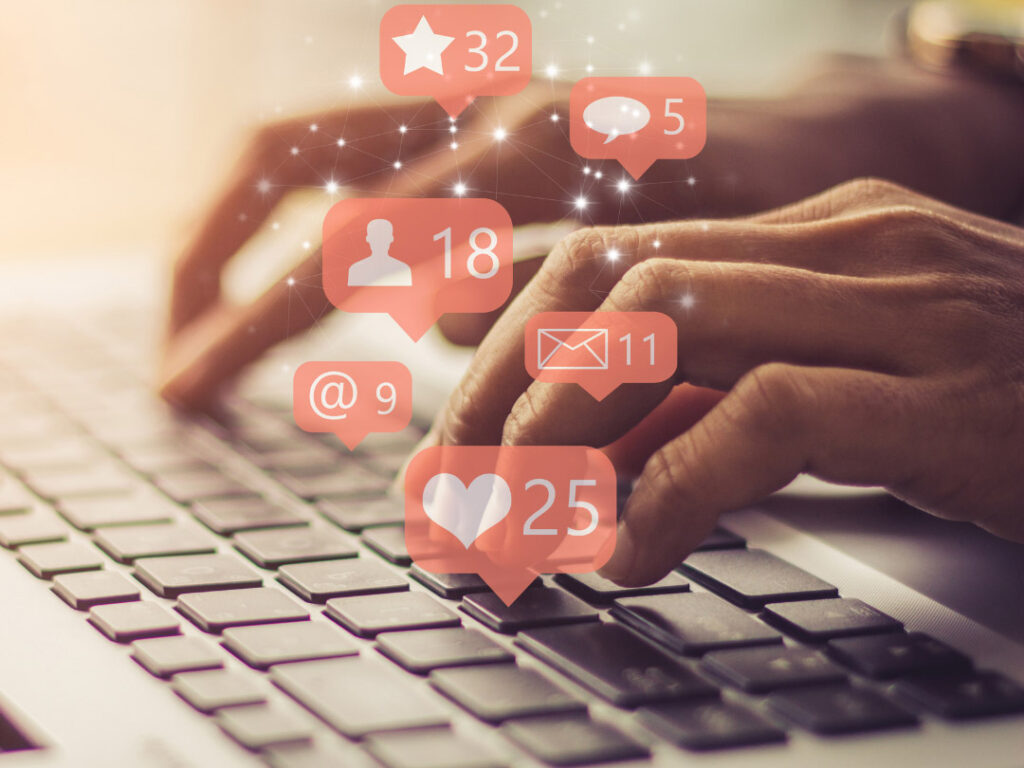 Hand auf einer Computer-Tastatur, darüber orange Social-Media-Bubbles mit Icons und Zahlen wie 32, 25, 18, 11 – Top Social Media Überschriften