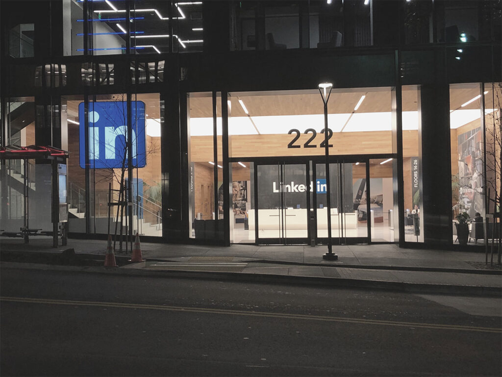 Außenansicht des LinkedIn-Logos mit blauem Schriftzug am Eingang, moderne Architektur und beleuchtete Schaufenster im Dunkeln bei Nacht